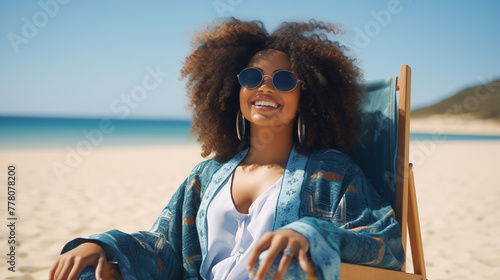 Happy young black woman relaxing on deck chair at beach wearing spectacles. Smiling african american girl with sunglasses enjoy vacation. Carefree happy young woman sunbathing at sea photo