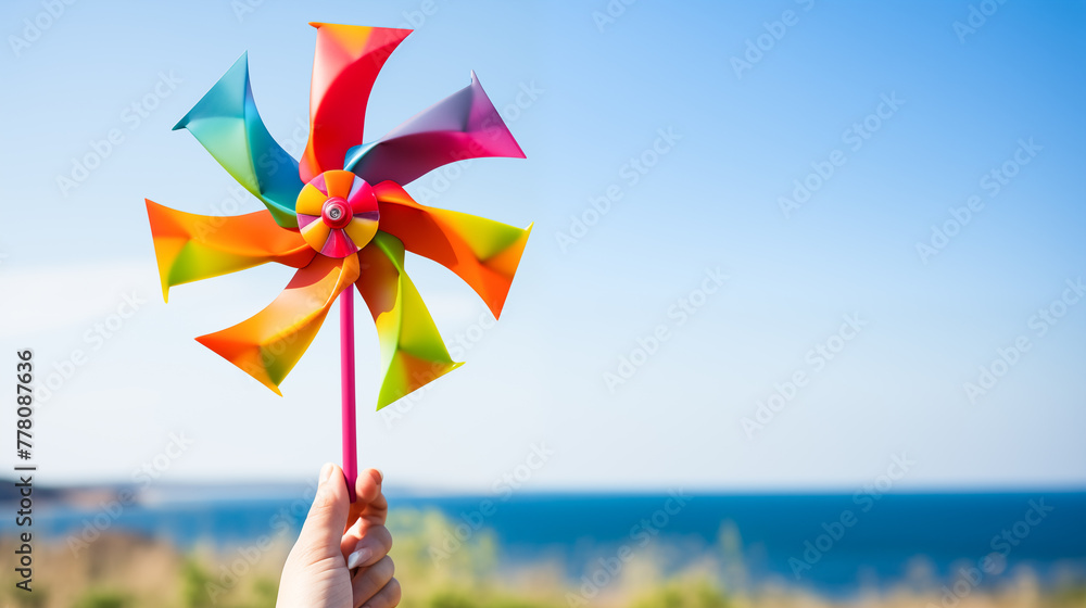Hand holding a windmill rotating colored plastic with blowing wind against a blue sky with green energy concept. Symbol of freedom and life Hand holding a windmill rotating colored plastic with blowing wind against a blue sky with green energy concept. Symbol of freedom and life