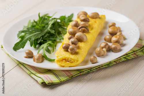 Close up French three eggs omelette with mushrooms, arugula for a breakfast on a white plate on wooden background. Low carb diet.