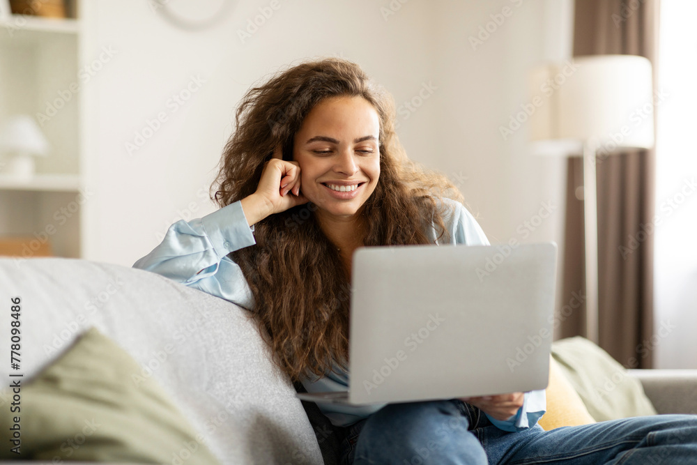 Young woman working on laptop computer while sitting on comfy sofa at home. Technology woman concept alternative office freelance Young woman working on laptop computer while sitting on comfy sofa at home. Technology woman concept alternative office freelance