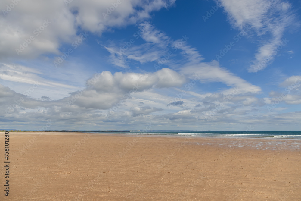 At St Andrews Beach in Scotland, the golden sands stretch far into the distance, merging seamlessly with the clear blue sea under a dynamic sky