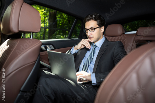 Successful handsome businessman sitting in the passenger seat in his luxury car working on laptop and driving to a business meeting © Vitaliy