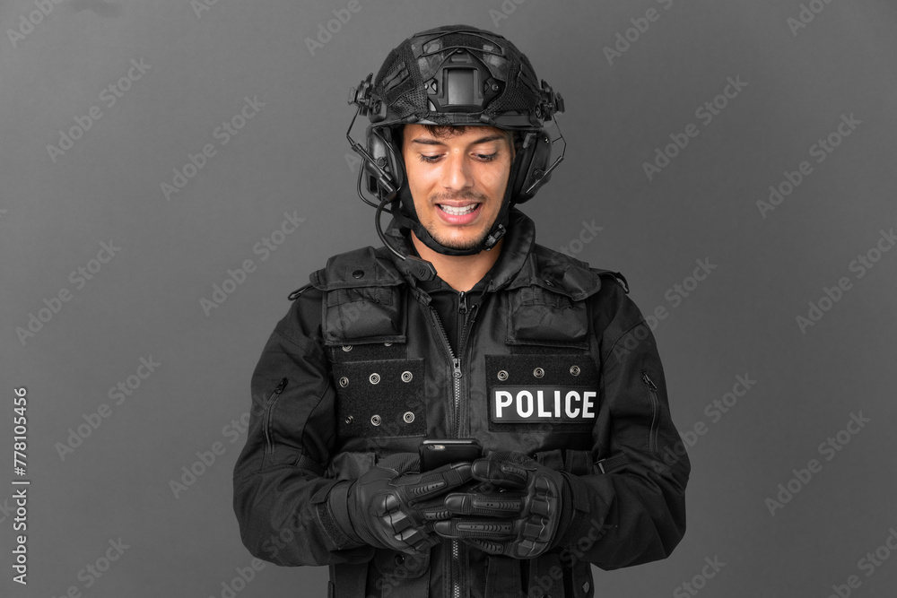SWAT caucasian man isolated on grey background sending a message with the mobile SWAT caucasian man isolated on grey background sending a message with the mobile