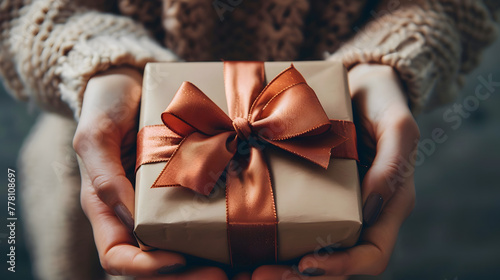 Women's hands hold an elegant gift box. The gift is wrapped in wrapping paper and decorated with a bow. The photo was taken in high resolution. It is a very detailed