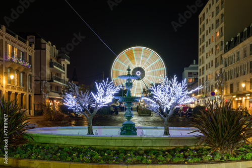 Grande roue illuminée en jaune devant une fontaine la nuit à Noël