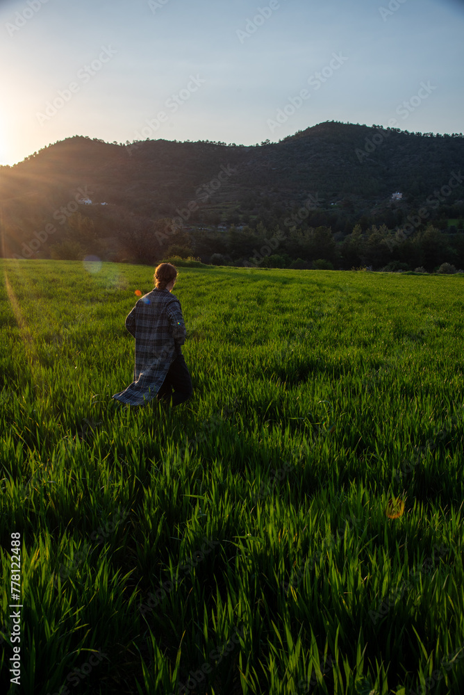 Woman with long coat holding long hair enjoying sunset on the green meadow Woman with long coat holding long hair enjoying sunset on the green meadow