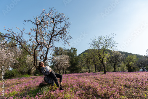 Young woman leaning and relaxing under almond blooming tree enjoying spring. © Michalis Palis