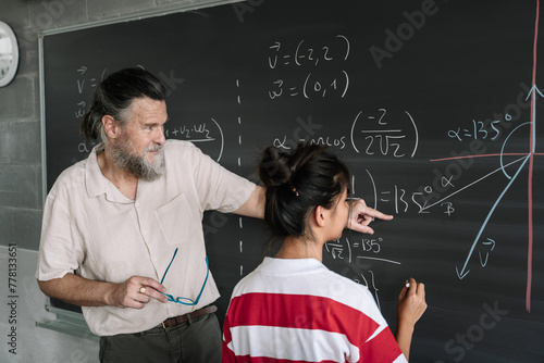 Young Female Asian Teenager Student doing Maths Exercises on Blackboard with help of the teacher in High School