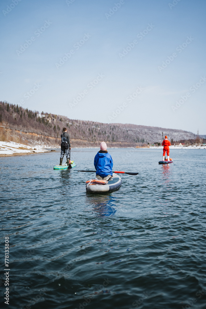 SUP boarders sailing on a mountain river, rear view of people standing on a board with a paddle, a team of athletes, outdoor activities on the water.