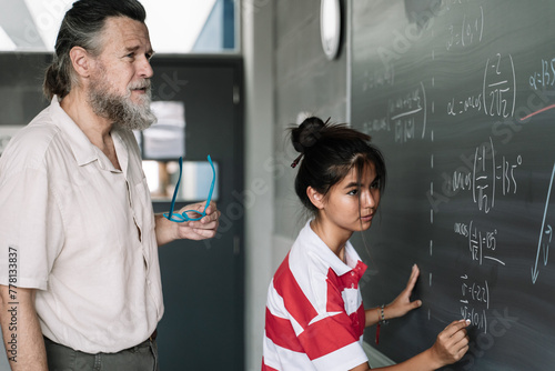 Female Asian Teenage Student Writing Maths Exercises on Blackboard with teacher supervision in Secondary School