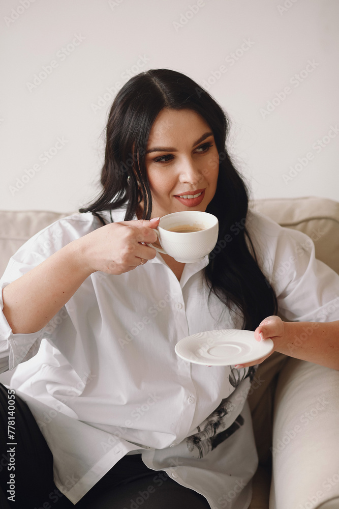Portrait of smiling brunette woman in white shirt enjoying a cup of coffee at home. Relax time. Peaceful lady having relaxing day Portrait of smiling brunette woman in white shirt enjoying a cup of coffee at home. Relax time. Peaceful lady having relaxing day