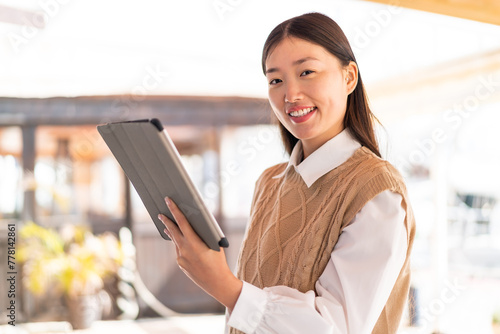 Young Chinese woman at outdoors holding a tablet with happy expression photo