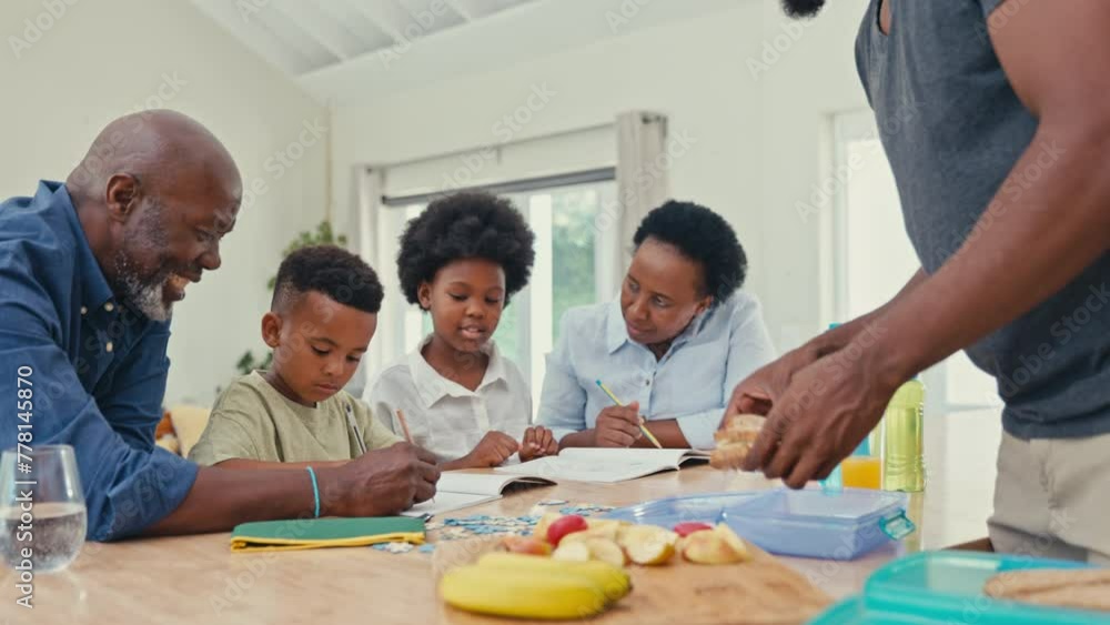 Multi-generation family helping children with homework sitting at table as father makes packed school lunch - shot in real time Multi-generation family helping children with homework sitting at table as father makes packed school lunch - shot in real time