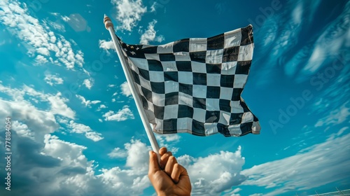 Hand waving a checkered race flag under blue skies.