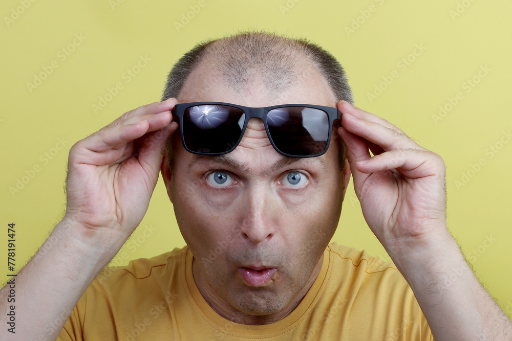 Studio shot of a man 40-50 years old, holding black glasses, looking surprised and funny, wearing a yellow T-shirt, against a yellow studio background. Studio shot of a man 40-50 years old, holding black glasses, looking surprised and funny, wearing a yellow T-shirt, against a yellow studio background.