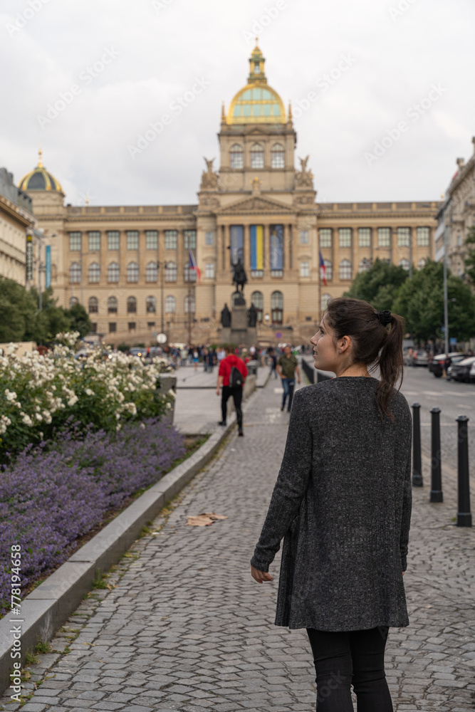 Unrecognizable female tourist with her back turned strolling in front of the Prague History Museum