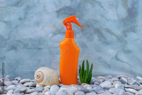 SPF. A bottle of sunscreen on the pebbly seashore is decorated with seashells. Sun lotion. UVA UVB. Body care. Blue background.