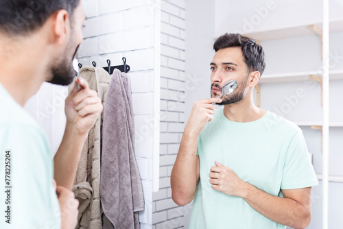 Handsome man doing facial workout with spoon exercises in front of the mirror. Young guy holding spoon with mouth