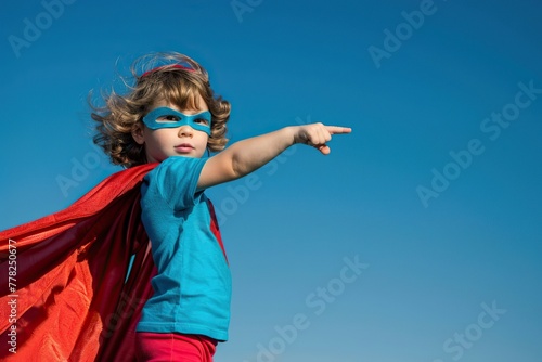 Child dressed as superhero with red cape extending arm on blue sky background