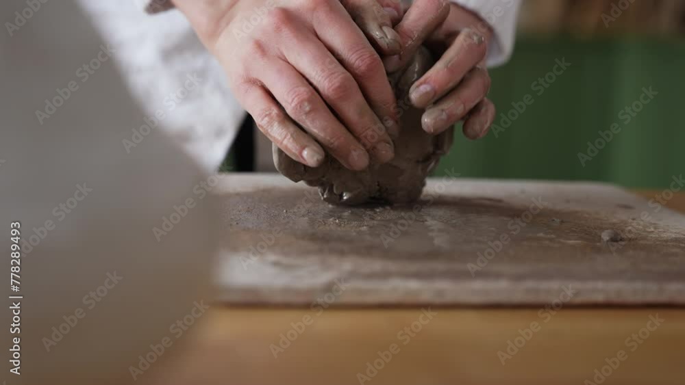 Potter's hands carefully holding and molding a piece of clay into form on a sandy pottery mat Potter's hands carefully holding and molding a piece of clay into form on a sandy pottery mat