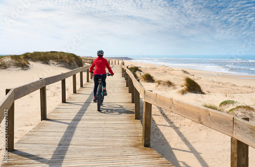 happy active senior woman cycling during moody golden hour at the beach of the atlantic coast of Aveiro, Portugal
