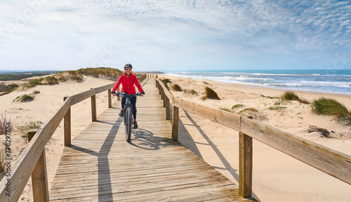 happy active senior woman cycling during moody golden hour at the beach of the atlantic coast of Aveiro, Portugal © Uwe