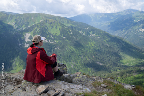 Woman with backpack, hiking in the mountains, sitting on the rock looks at the valley from the High Tatras. Sunny summer day with rain clouds in the distance.