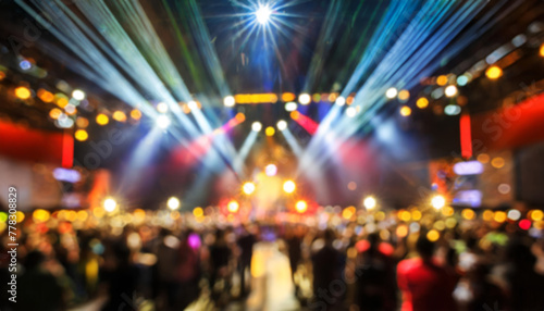 Blurred image of indoor music concert, with audience, stage and colored lights. People at a concert. Live music, leisure concept. Blurred background for social media content.