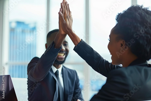 Successful business people giving each other a high five in a meeting. Two young business professionals celebrating teamwork in an office photo