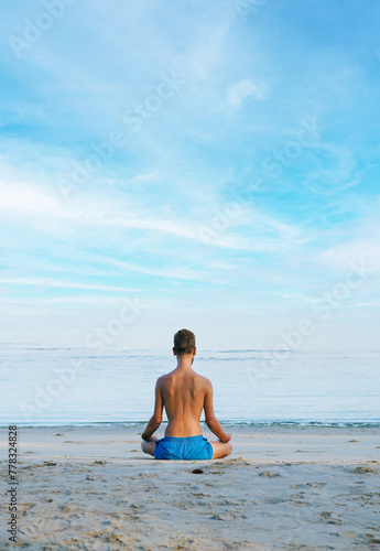 Man meditates or doing yoga exercise on the sandy beach in the morning. View from the back. Vertical.