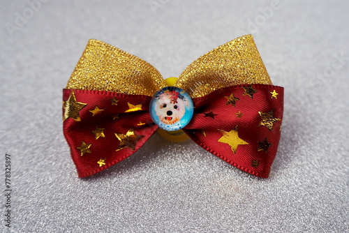 On a gray shiny background there is a red bow with stars with glued rhinestones and an insert in the middle with a white dog. accessories for pets. Top notes for long hair on the head. front view