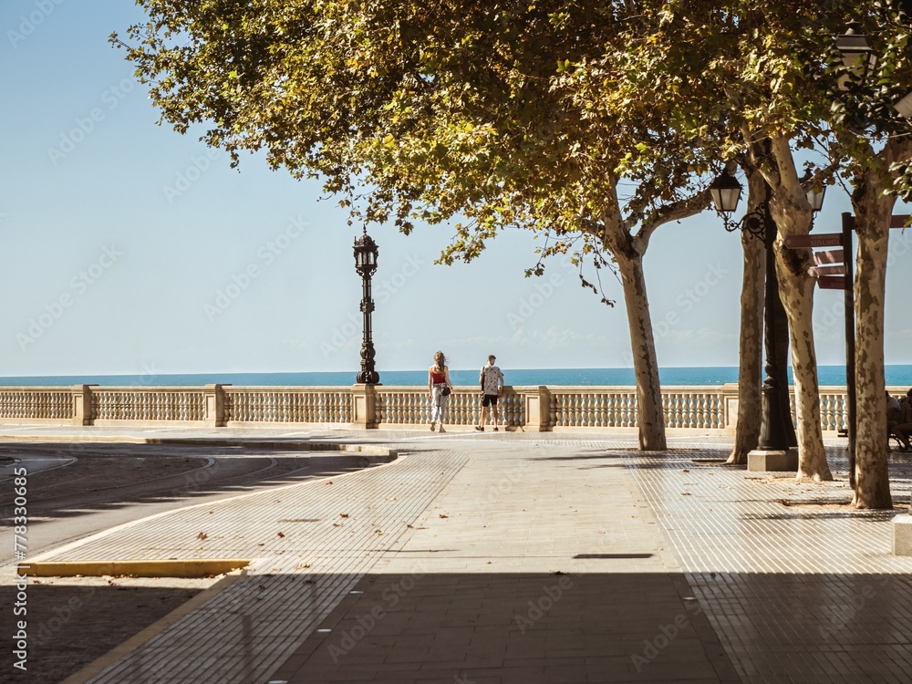 A tourist couple walking on the seaside beach promenade of Cadiz under trees and lanterns