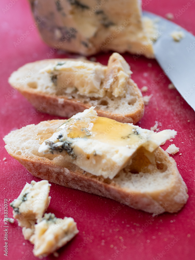 Stilton Blue Cheese with a drizzle of Honey on a French Baguette. Red Cutting Board. Stilton Blue Cheese with a drizzle of Honey on a French Baguette. Red Cutting Board.