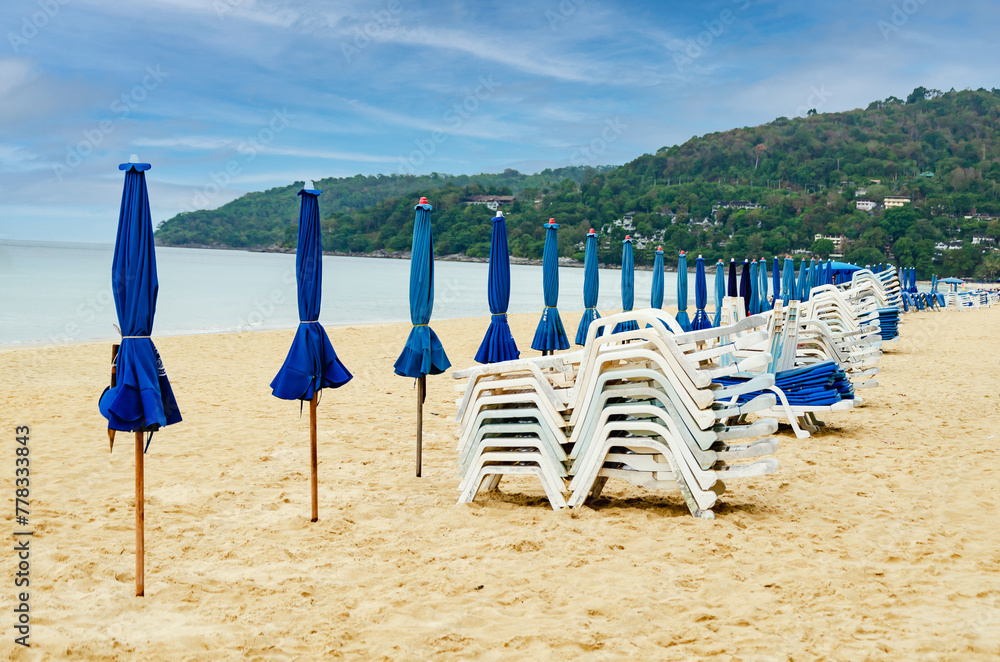 Folded beach umbrellas and sun loungers on an empty beach on cloudy day