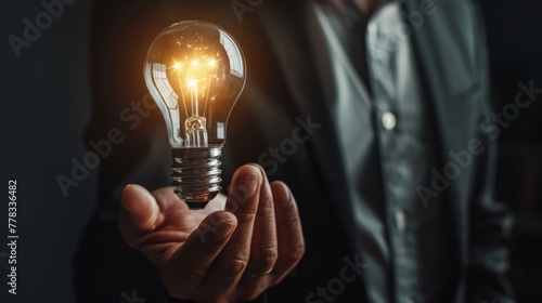 Hand holding a glowing light bulb on a dark background. Innovation and idea concept for design and print