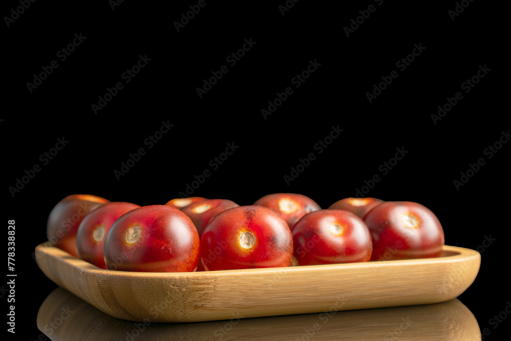Several black cherry tomatoes on a bamboo plate, macro, isolated on black background. Several black cherry tomatoes on a bamboo plate, macro, isolated on black background.