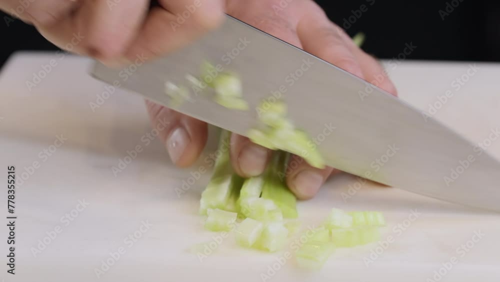 The cook cuts celery stalks with a large kitchen knife into small slices. Metal knife chopping celery on a gray plastic board on kitchen table. 4k slow motion video. The cook cuts celery stalks with a large kitchen knife into small slices. Metal knife chopping celery on a gray plastic board on kitchen table. 4k slow motion video.