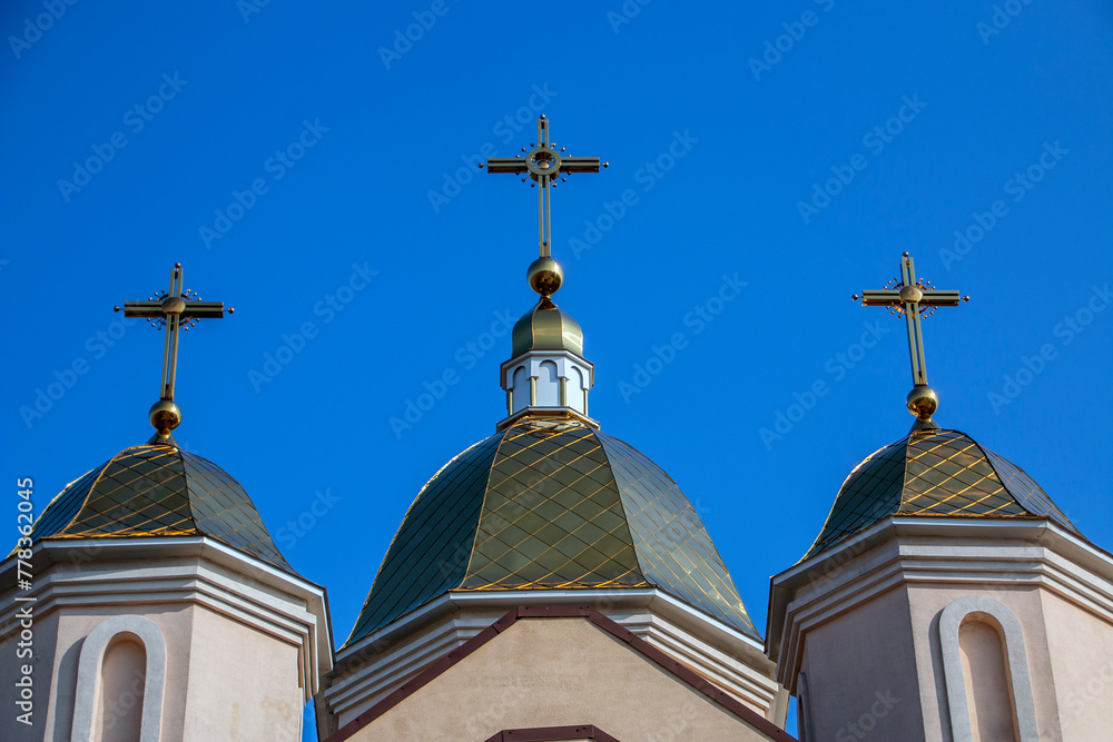 Three domes of the church with holy crosses against a clear blue sky