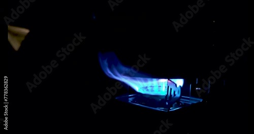 Bright blue flames from a camp gas stove with a camp pot filled with water at The dark night. outdoor camping.