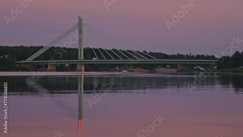 Lumberjack's Candle cable-stayed metal highway bridge in the Finnish Arctic capital city of Rovaniemi over the Kemijoki River in sunset colors in summer. Reflection of the bridge in the calm water. photo