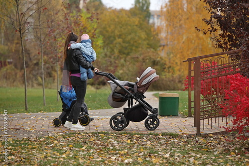 An young woman walks with a pram among the autoumn greenery. A governess is nursing a child on the street. Raising children zorovym and seasoned. Baby sleep in the fresh air. Socialization of family.