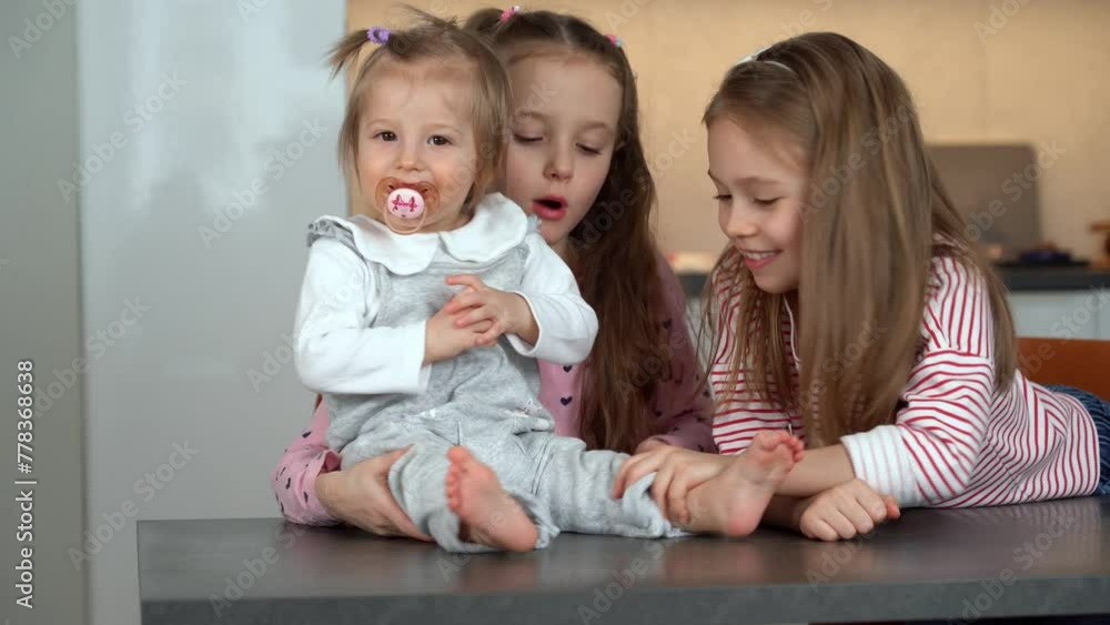 Sisters funny laugh playing with little baby at home. Girls looking after baby. Happy family concept. Active childrens games, leisure Sisters funny laugh playing with little baby at home. Girls looking after baby. Happy family concept. Active childrens games, leisure