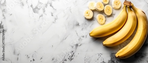   A few bananas are resting atop a marble countertop, alongside sliced chunks of banana photo