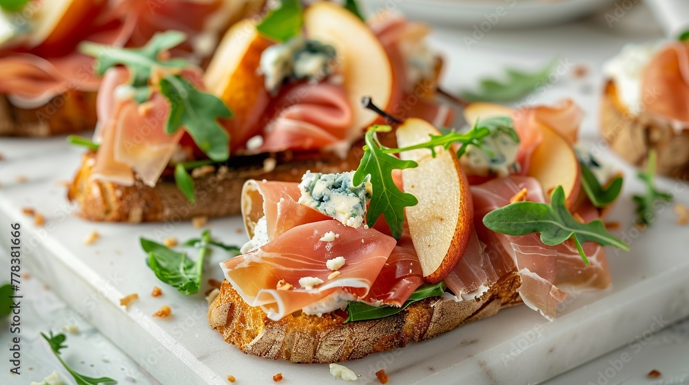 Delicious appetizer crostini, tapas, or open-faced sandwiches featuring pear, prosciutto, arugula, and blue cheese, elegantly arranged on a white marble board. T