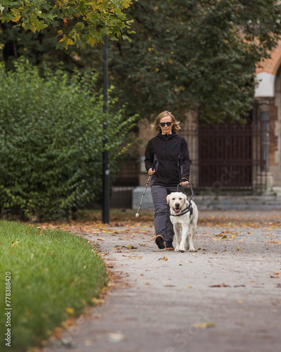 Visually impaired woman walking along city park with a guide dog assistance. Loyal companions for blind people concept.