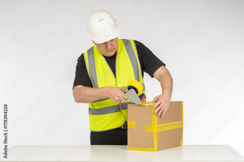 Man in Safety Gear Securely Taping a Box, Focused on Packaging in a Bright Work Environment Man in Safety Gear Securely Taping a Box, Focused on Packaging in a Bright Work Environment