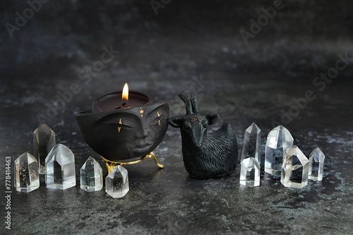 amulet in goat form, crystals and Magic shaman bowl with candle on table, dark background.  esoteric spiritual practice. witchcraft, mysterious ritual with quartz crystal towers.