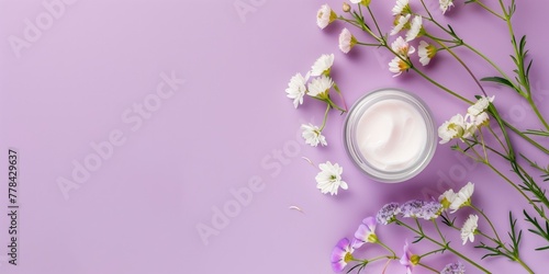 Face cream jar and flowers on purple background with blank space for tex, top view