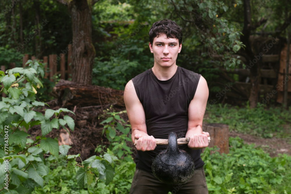 Young guy in the nature in the forest lifting a heavy weight on his biceps, the guy likes to exercise in the fresh air, avoids gyms and large crowds Young guy in the nature in the forest lifting a heavy weight on his biceps, the guy likes to exercise in the fresh air, avoids gyms and large crowds