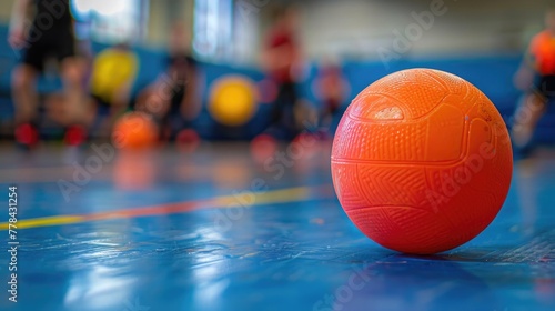 A close view of a soft, colorful dodgeball against the gymnasium floor with players in action blurred in the background, showcasing the fun and teamwork of dodgeball